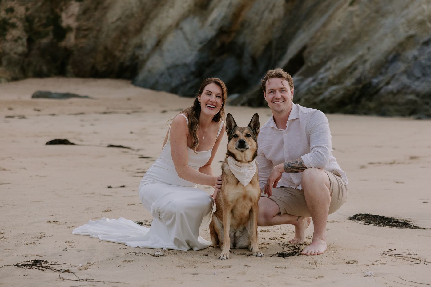 Kelly and Martin crouching on the sand with their dog Poppy on their wedding day